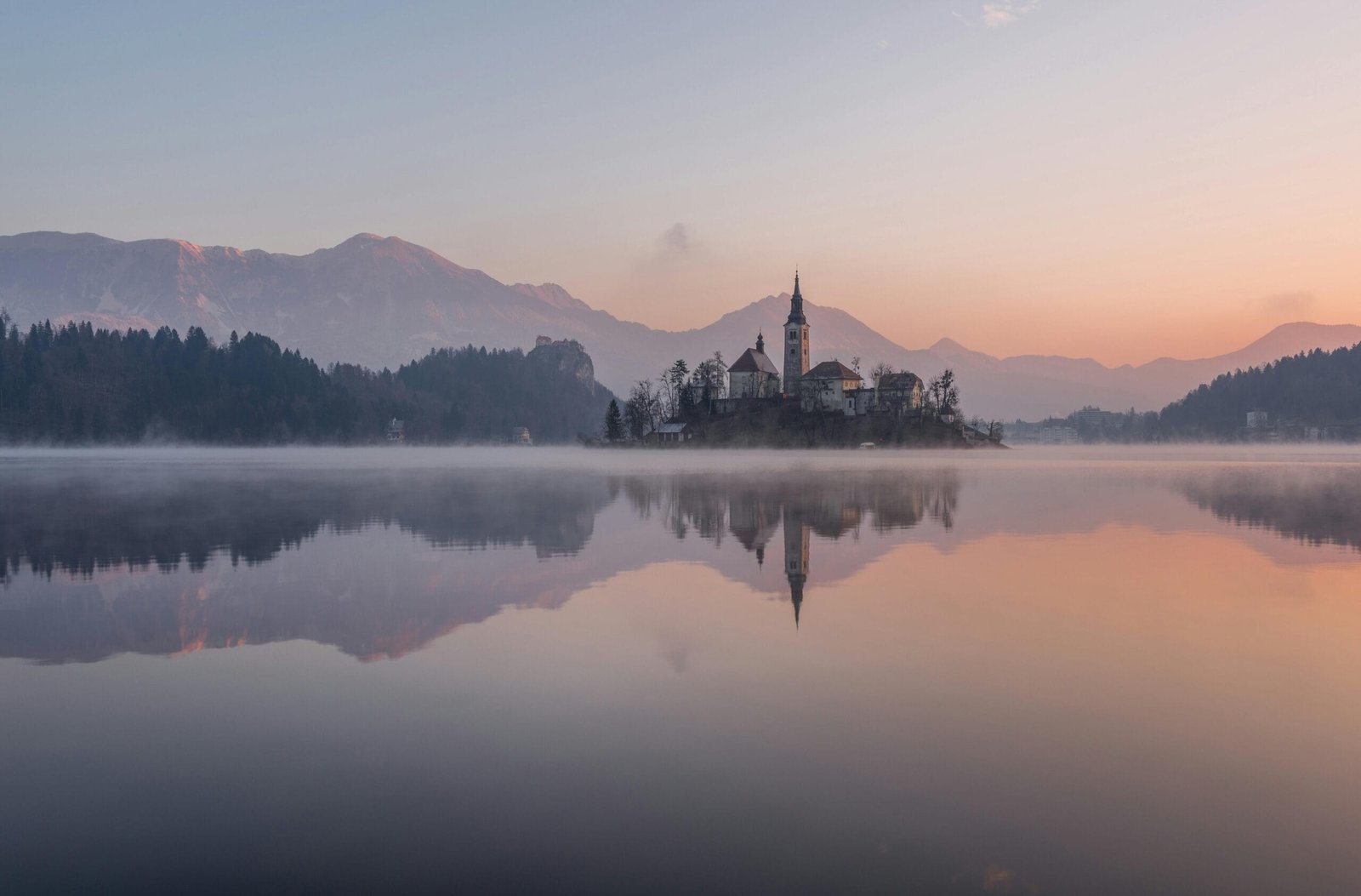 Tranquil morning view of Lake Bled with misty reflections and church silhouette.