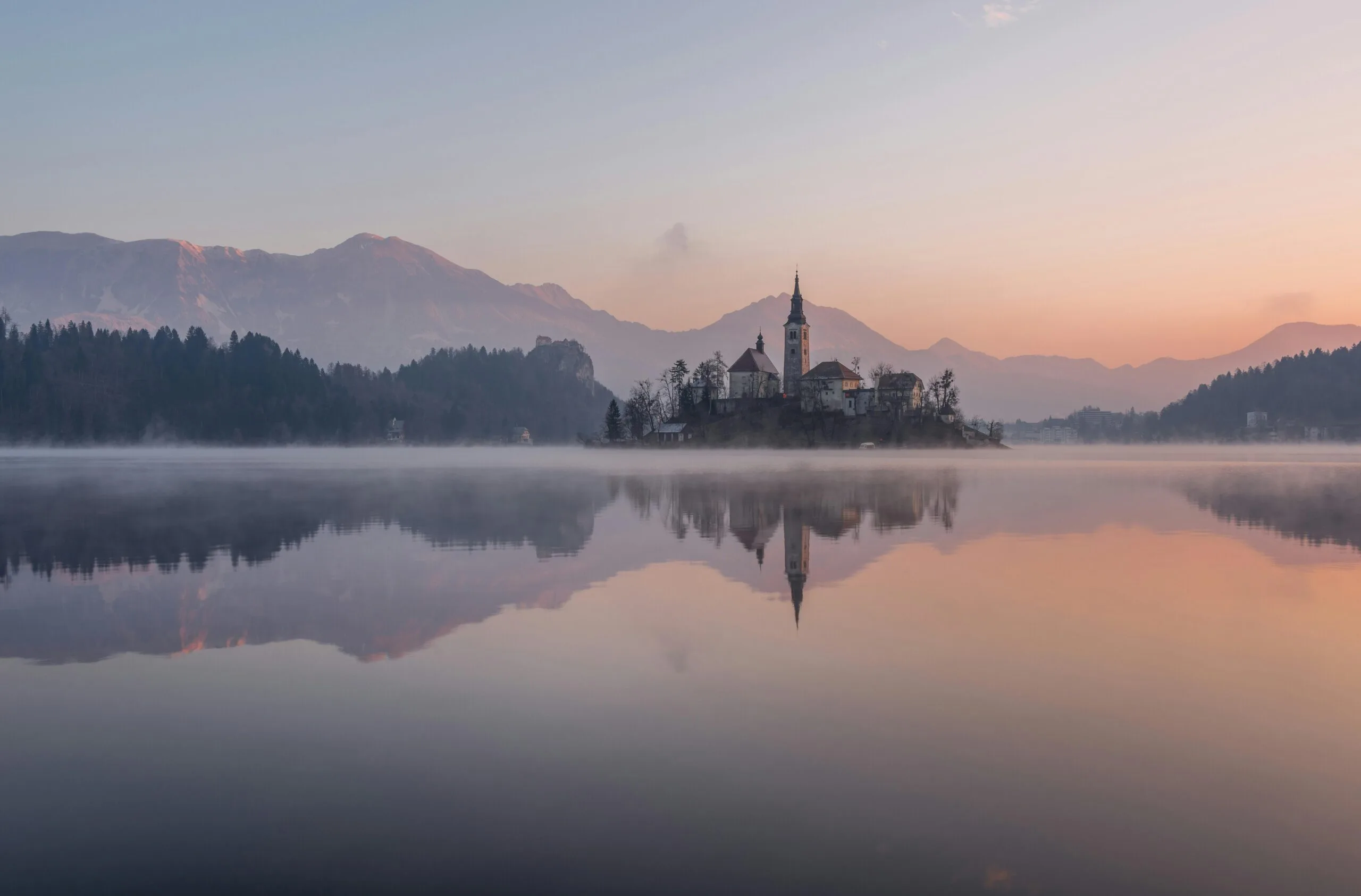 Tranquil morning view of Lake Bled with misty reflections and church silhouette.